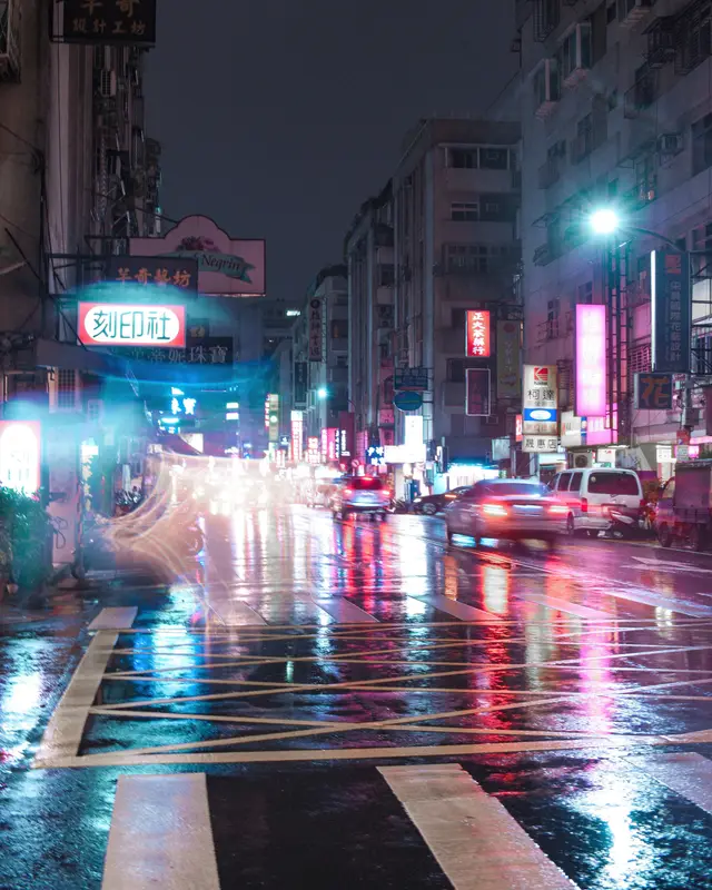 雨後的街口，霓虹招牌倒映在濕掉的柏油路上